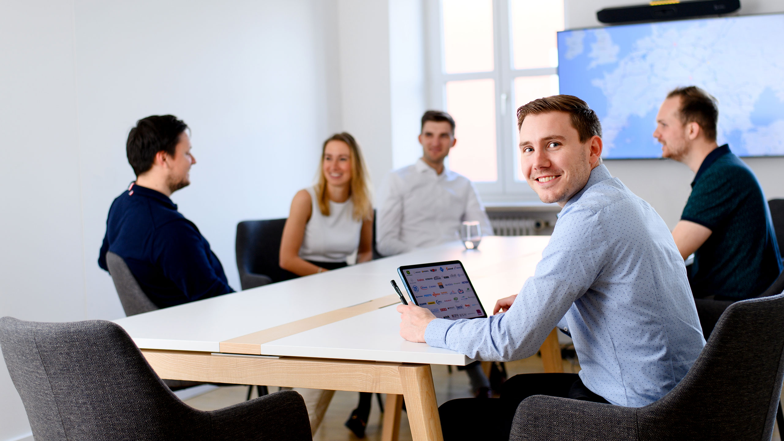 Headerbild zur Karriere-Seite für Berufseinsteigende: Gruppe aus fünf Personen aus dem Rothbaum-Team arbeitet bei guter Stimmung im Besprechungsraum im Office.